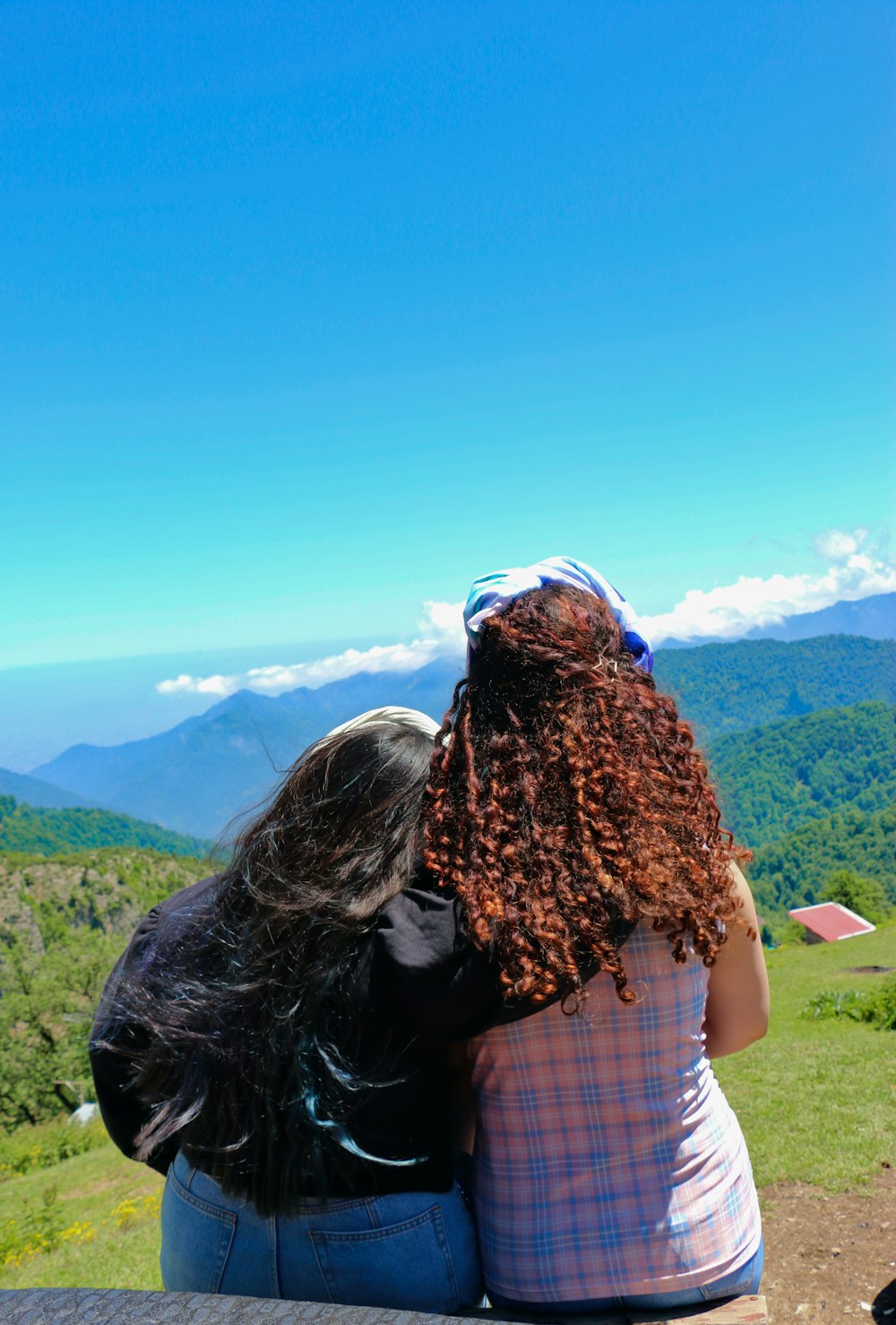 two people sitting on a ledge overlooking a valley with mountains in the background