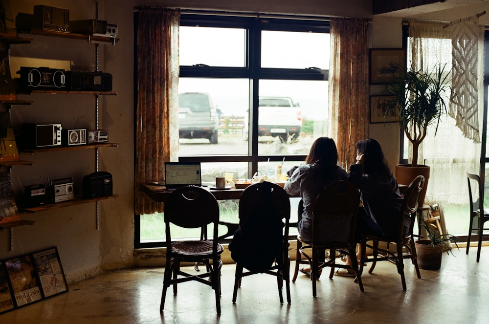 a couple of people sitting at a table in a room with a large window