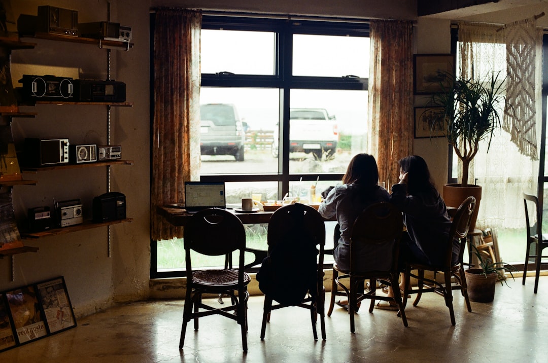 a couple of people sitting at a table in a room with a large window,
