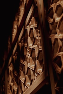 Wooden panels with intricate geometric patterns, featuring interlocking hexagons and star motifs. The craftsmanship is detailed, highlighting the three-dimensional nature of the carvings. The play of light and shadow enhances the texture and depth of the artwork.