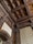 A detailed view of an ornately carved wooden ceiling with intricate patterns and designs. The woodwork includes floral and geometric motifs, covering the ceiling and archway. The walls feature elegant patterned wallpaper in a sophisticated setting.