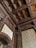A detailed view of an ornately carved wooden ceiling with intricate patterns and designs. The woodwork includes floral and geometric motifs, covering the ceiling and archway. The walls feature elegant patterned wallpaper in a sophisticated setting.
