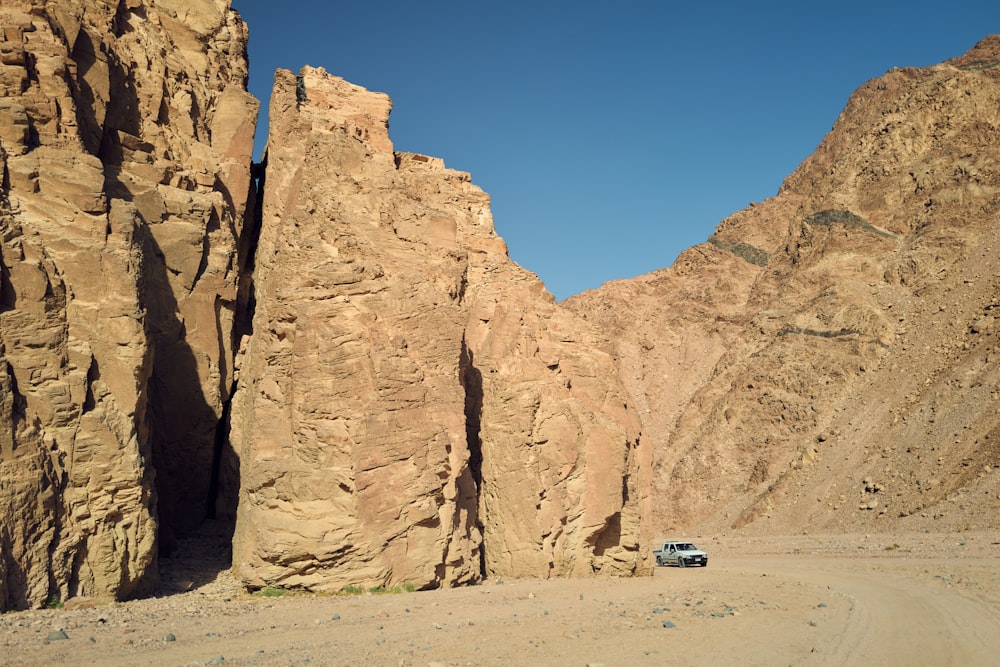 a car driving on a dirt road between large rocky cliffs