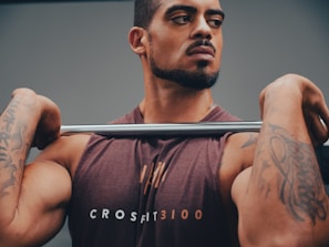 A CrossFit athlete mid-snatch, muscles engaged, with red wolf weightlifting logo visible on their shirt.