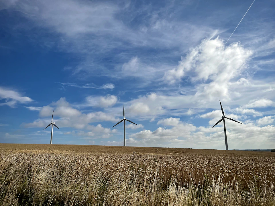Three wind turbines stand against a clear blue sky with angled blades and fluffy clouds