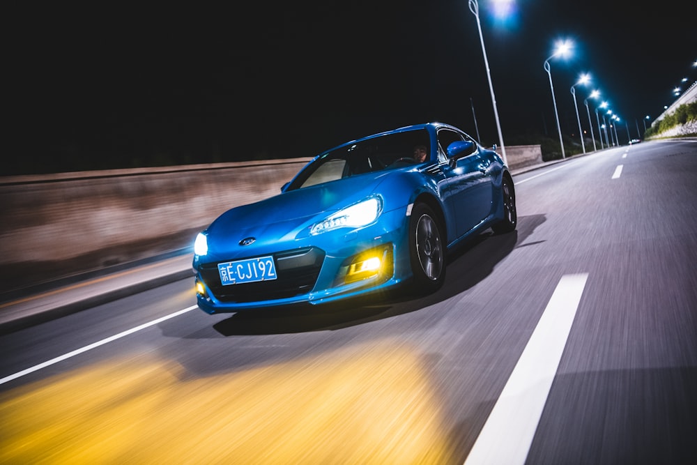 a blue sports car driving on a road at night