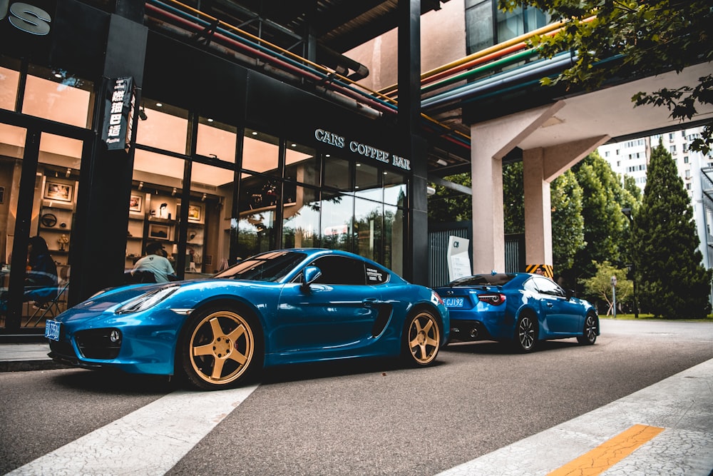 a couple of blue sports cars parked outside a building