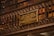 A library wall filled with books on shelves, with a detailed and ornate metal railing in front. Mounted on the rail is a plaque dedicated to Machado de Assis, a Brazilian writer, commemorating his memory.