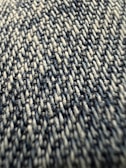 Close-up view of a textured fabric with tightly woven fibers, exhibiting a pattern of interlocking threads in varying shades.