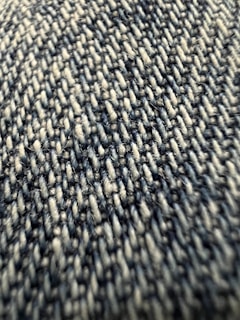 Close-up view of a textured fabric with tightly woven fibers, exhibiting a pattern of interlocking threads in varying shades.