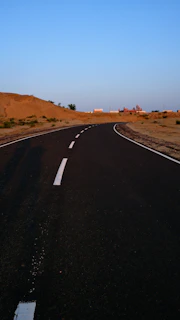 A winding desert road leading to a distant oasis surrounded by dunes