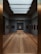 A modern art gallery with dim lighting features paintings displayed on dark gray walls. The room has a sleek design with wooden floors and a skylight that provides soft, natural lighting. The artworks are framed in dark colors, adding contrast to the space.