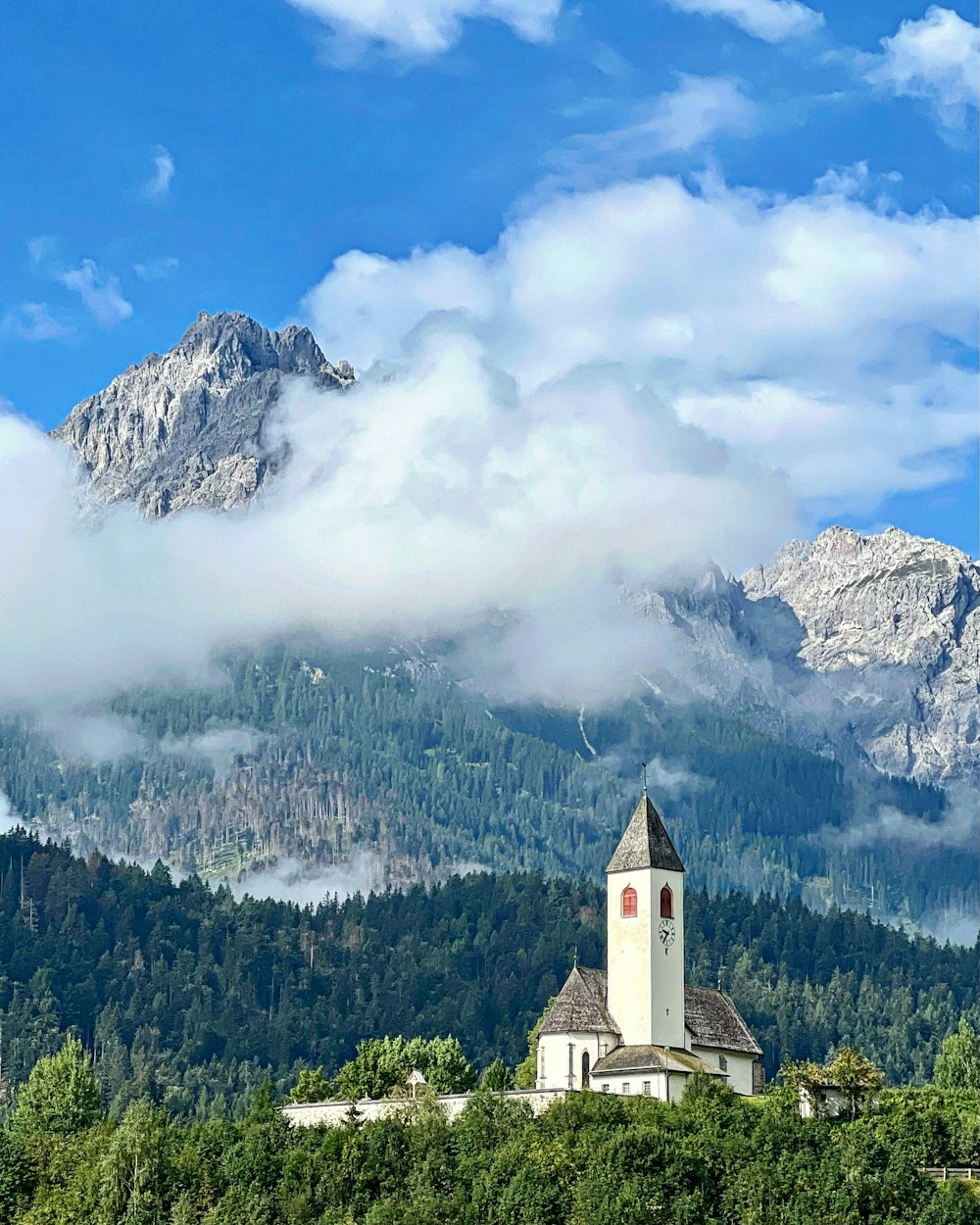 a building on a hill with clouds above it and mountains in the background