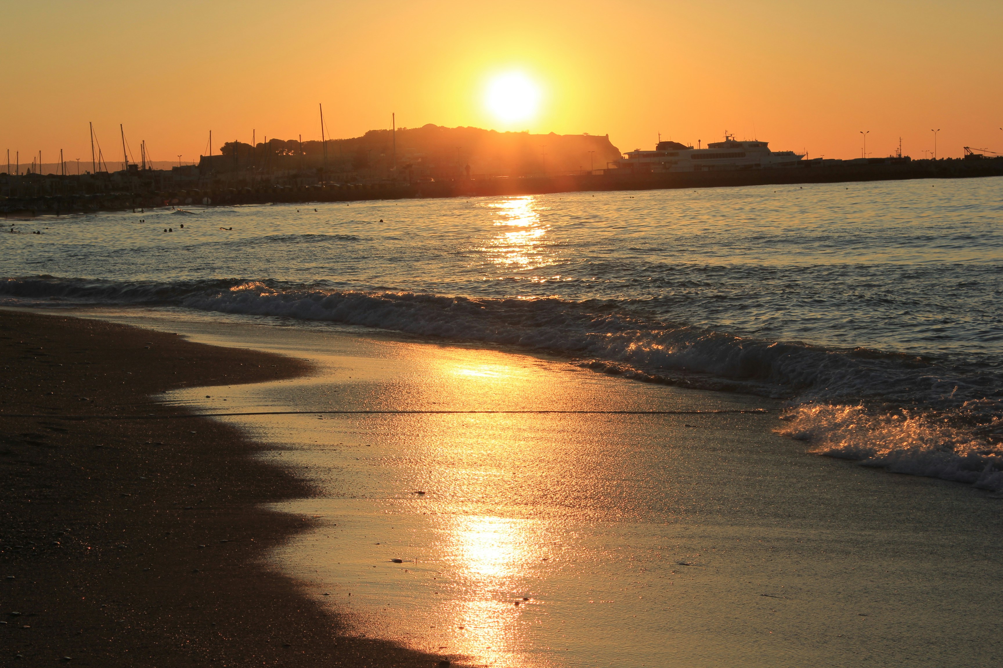 a beach with waves and the sun setting