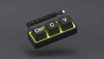 A stylized depiction of three raised keyboard keys labeled Ctrl, C, and V, set against a dark, neutral background. The keys are illuminated with a vibrant yellow glow, and a coiled USB cable is attached to the top of the keys.