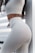 A person wearing a form-fitting, light-colored outfit featuring high-waisted leggings and a crop top. An eagle tattoo is visible on their waist, and the background includes a striped pattern.