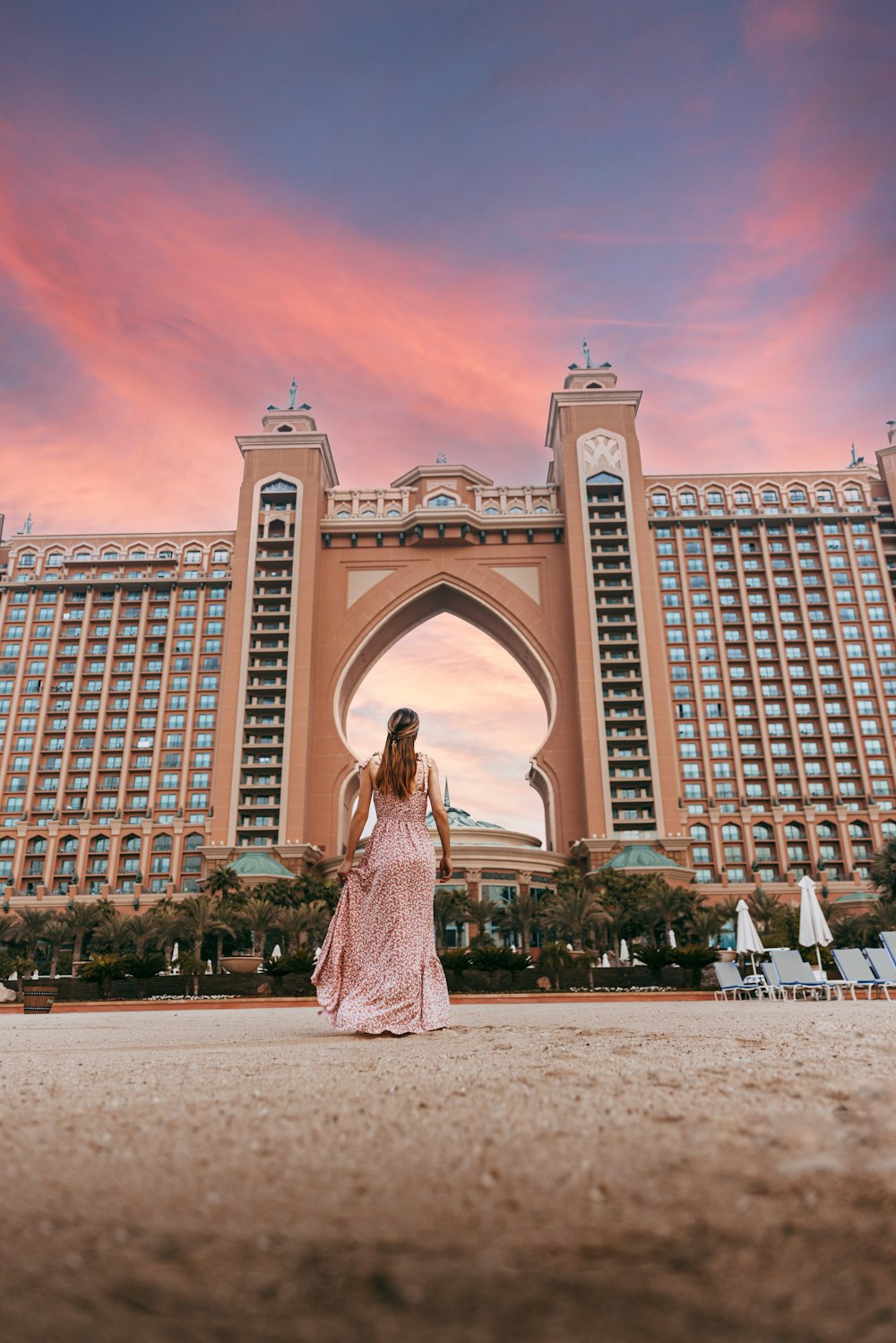 a person in a dress standing in front of a large building with Atlantis, The Palm in the background