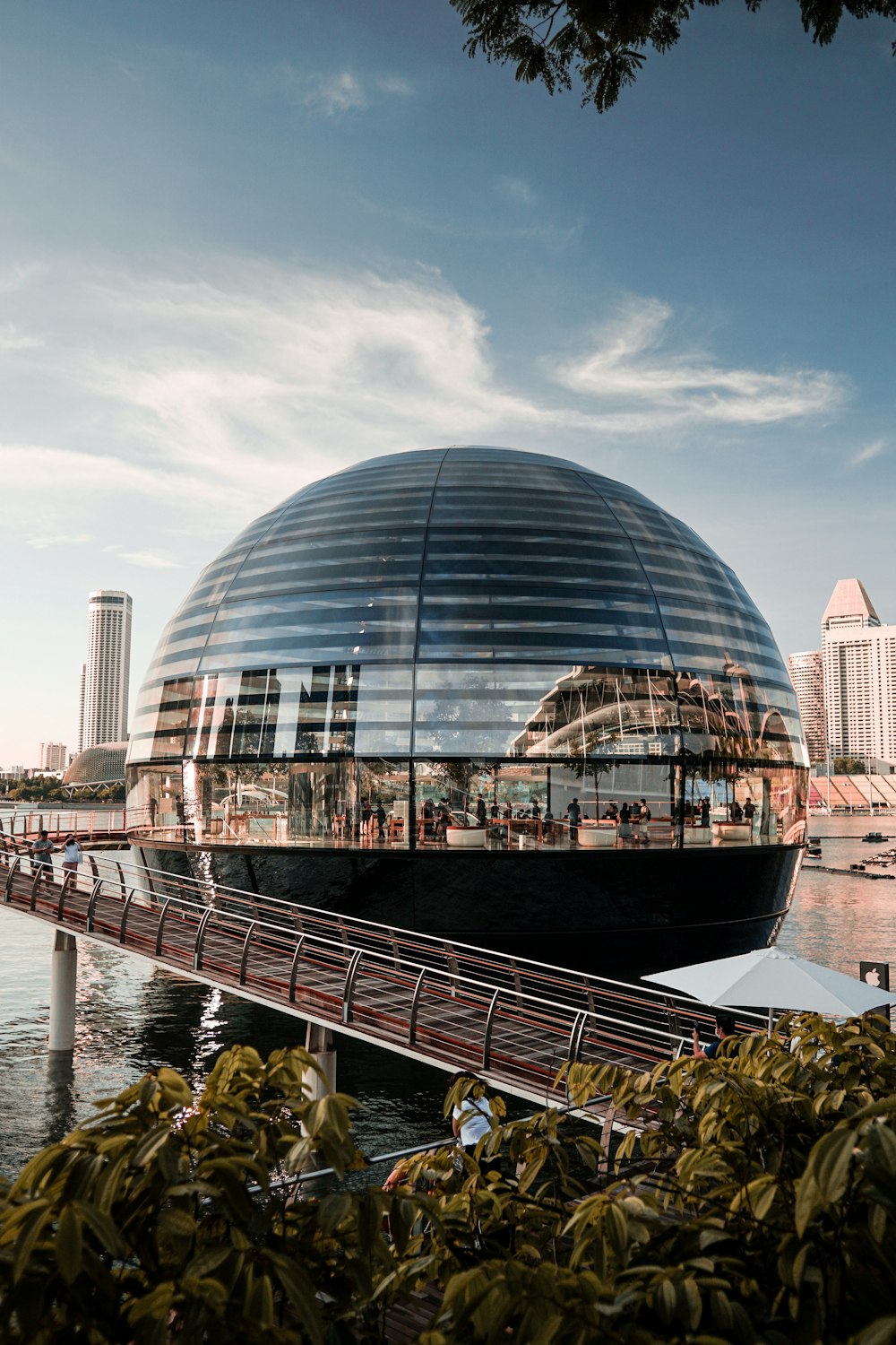 a large glass building with a bridge over a body of water