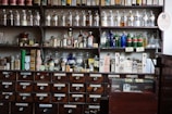 Shelves filled with labeled bottles and raw materials in a clean pharmacy lab.