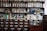 Shelves filled with an array of vintage apothecary bottles and containers, labeled with various substances and remedies. Glass jars and bottles of different shapes and colors, including clear, blue, and amber, are displayed neatly. Below the shelves, a set of wooden drawers, each labeled with different chemical or herbal names, completes the typical old pharmacy look.