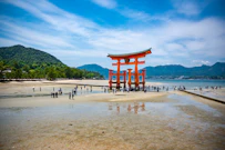 a large red structure on a beach with Itsukushima in the background