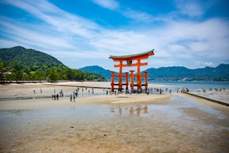 a large red structure on a beach with Itsukushima in the background
