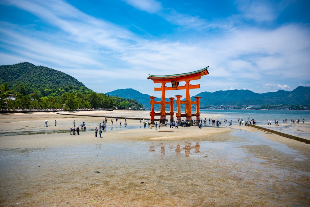 a large red structure on a beach with Itsukushima in the background