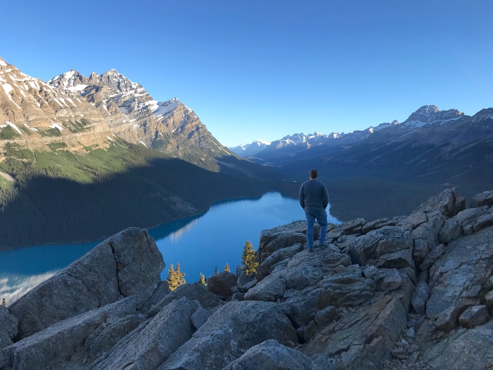 a man standing on a rocky ledge overlooking a lake and mountains