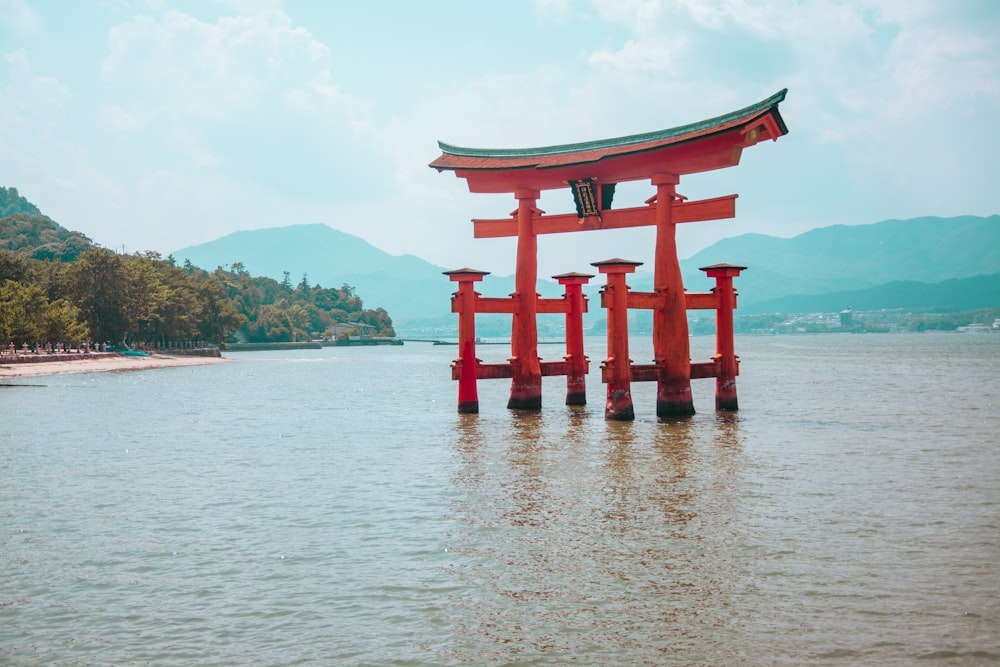 a red structure in the middle of a body of water with Itsukushima in the background