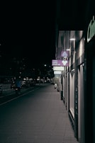 A quiet street at dusk with warm lights glowing from windows and a single bicycle leaning against a fence.