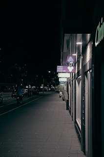 A quiet street at dusk with warm lights glowing from windows and a single bicycle leaning against a fence.
