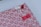 A beautifully wrapped package features a decorative patterned paper with small, red floral designs on a pink background. The package is adorned with three intricate knots in red and white string, finely detailed and placed thoughtfully. A small red strip of tape holds part of the arrangement together.