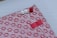 A beautifully wrapped package features a decorative patterned paper with small, red floral designs on a pink background. The package is adorned with three intricate knots in red and white string, finely detailed and placed thoughtfully. A small red strip of tape holds part of the arrangement together.