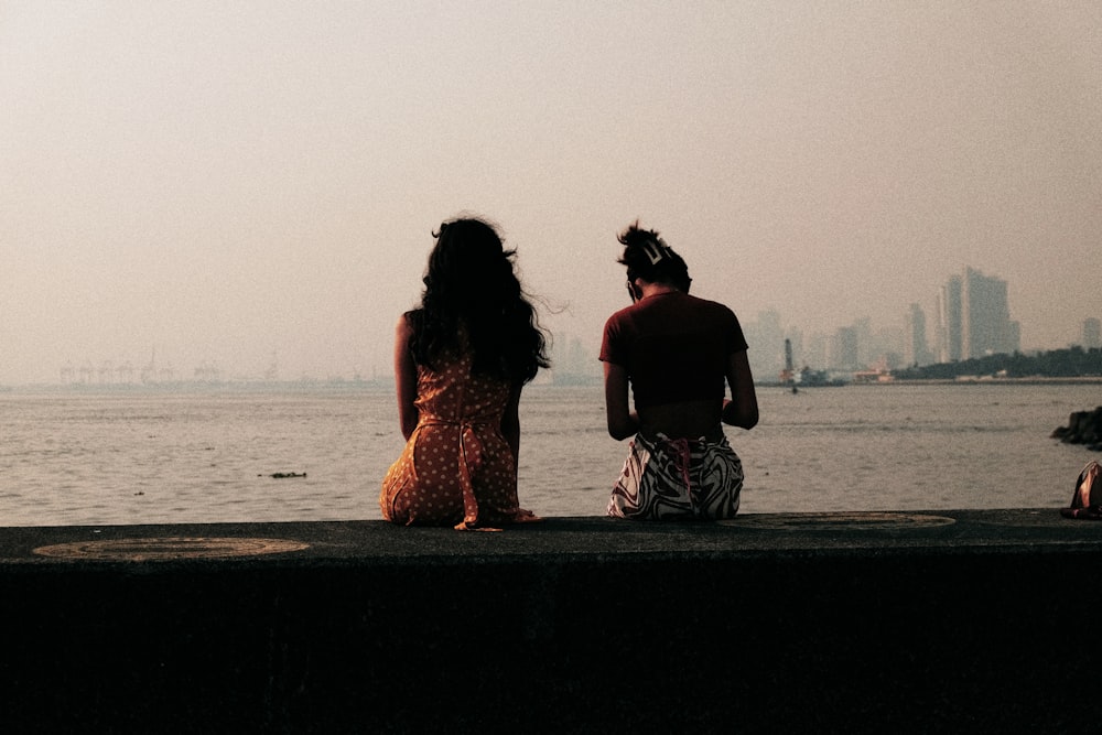 a man and woman sitting on a ledge looking at the water