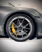 A close-up view of a sleek, modern car tire with a detailed alloy wheel design. The wheel features a vibrant yellow brake caliper visible through the spokes, while the tire brand and specifications are embossed along the sidewall.