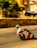 A motorcyclist in colorful racing gear leans into a sharp turn during a high-speed street race. The blurred background suggests motion, with hay bales serving as a barrier on the side of the road. Buildings and trees line the street, adding an urban feel to the race setting.