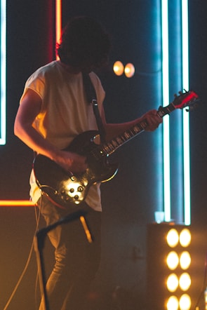 Close-up of a musician playing electric guitar under pink and purple neon lights on a dark background
