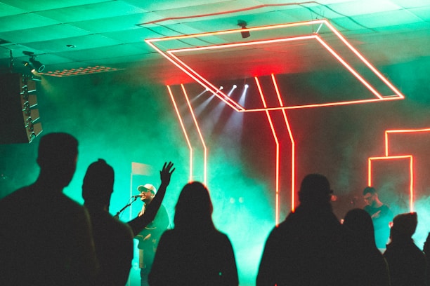 A lively crowd enjoying live music on stage with neon lights casting colorful glows in a dark bar setting.