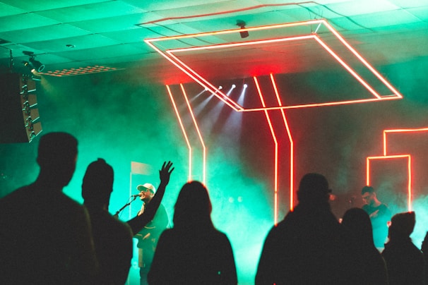 An artist performing live on stage, surrounded by neon visuals.