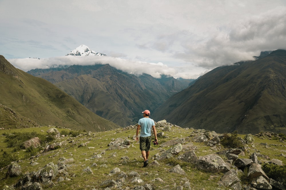 a man standing on a rocky hill with mountains in the background