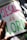 A hand-drawn illustration features the words 'JESUS is LORD' written in large, colorful letters on a sheet of paper. The word 'JESUS' is in pink, 'is' is in orange, and 'LORD' is in green. The paper is resting on a surface that appears to be covered in artistic materials, hinting at an artistic setting. A hand is visible, possibly holding a green marker.