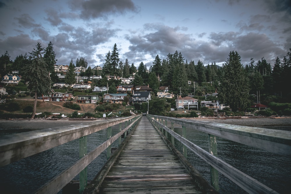 a wooden bridge over water with houses and trees in the background