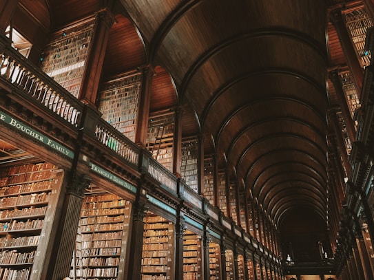 An expansive and ornate library interior with high arched ceilings and numerous rows of bookshelves filled with books. The architecture features intricately designed wooden beams and balconies, creating a sense of grandeur and history.