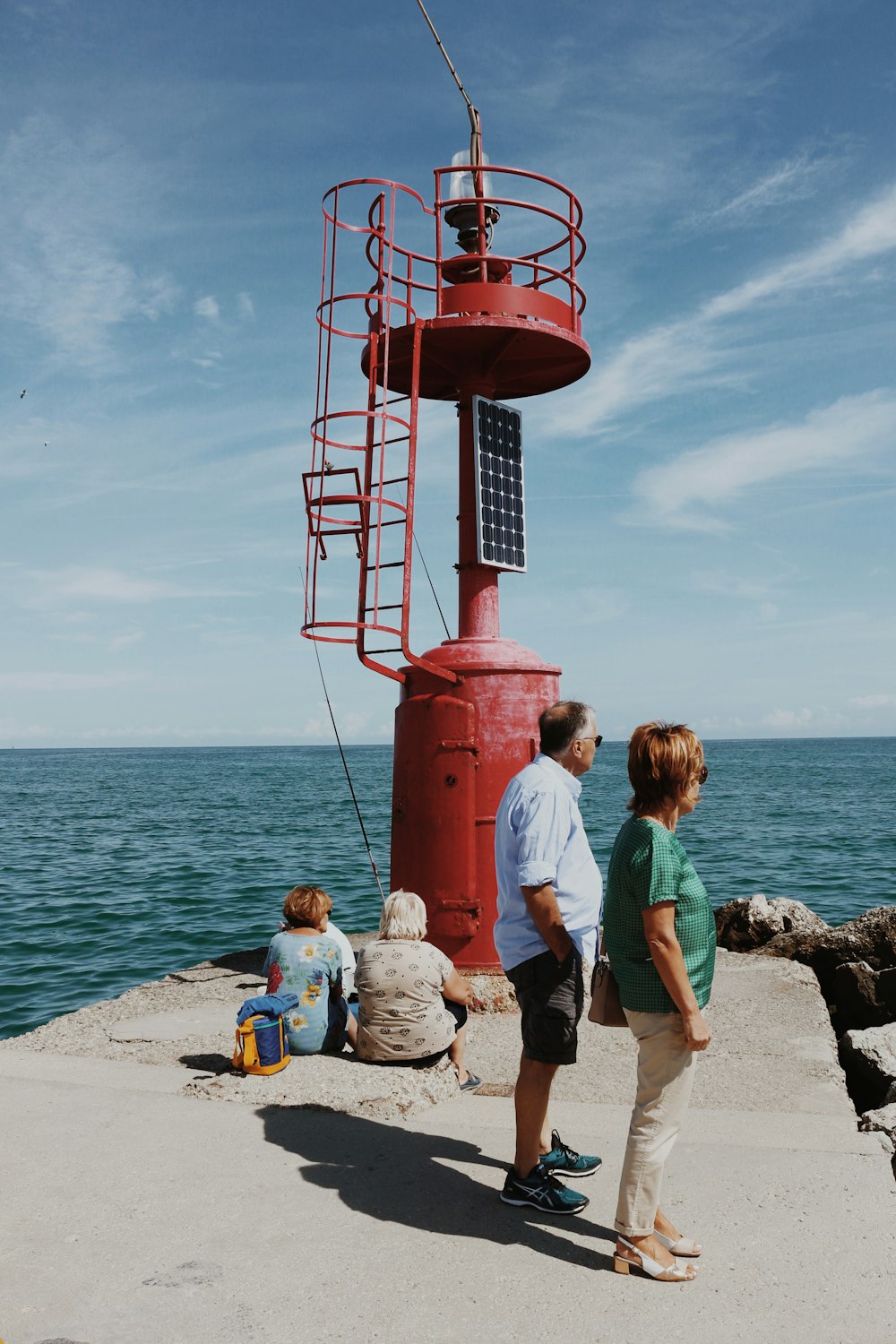 um grupo de pessoas em pé em uma praia olhando para uma torre vermelha