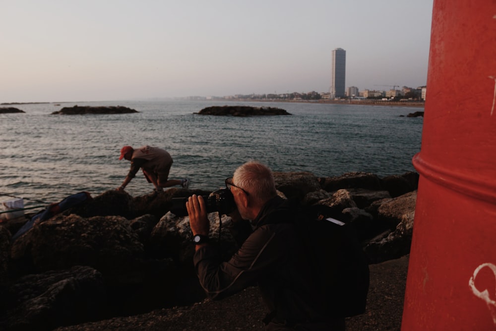 a man taking a picture of another man on a rocky beach
