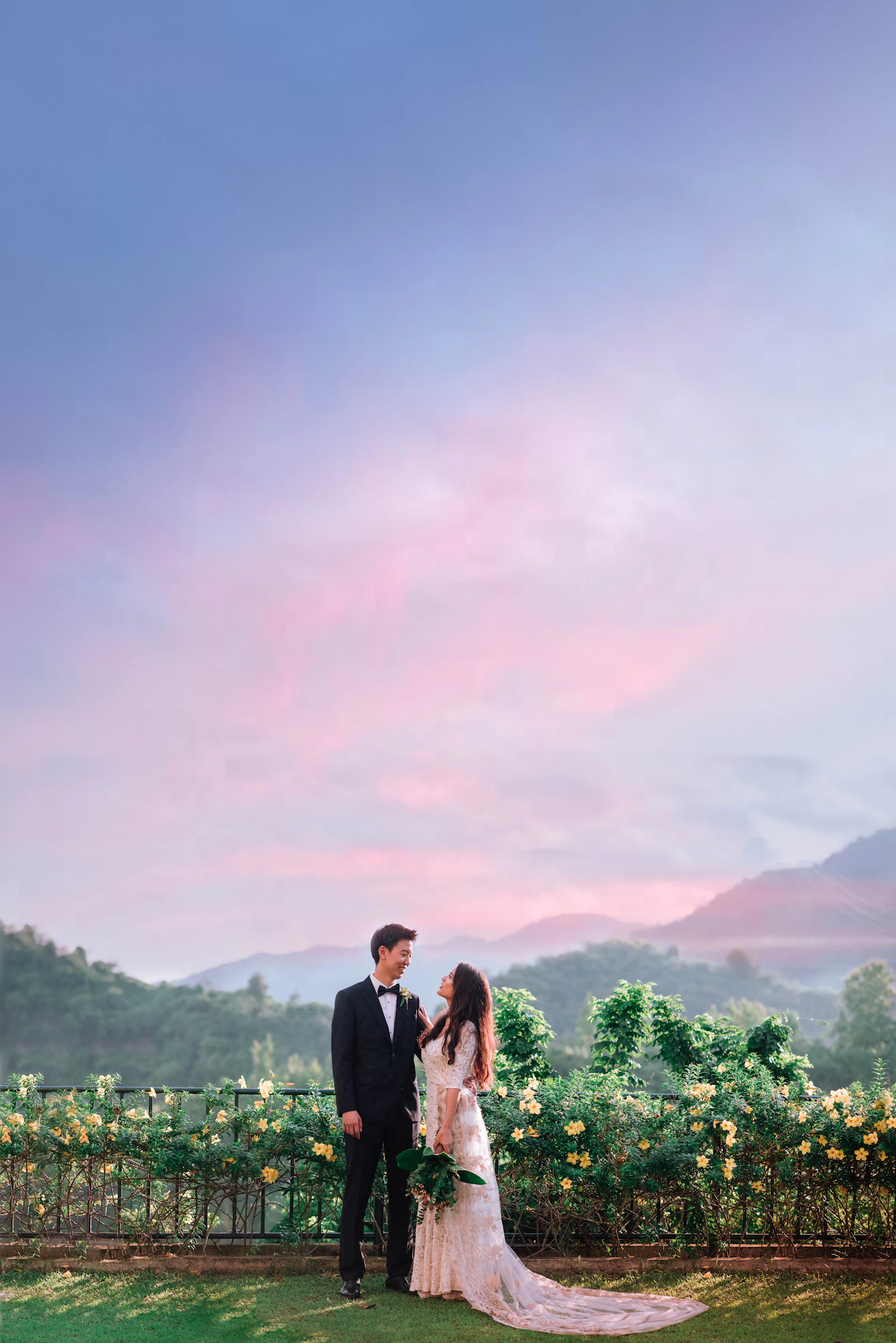 A couple in wedding attire standing in front of a vineyard in warm evening light