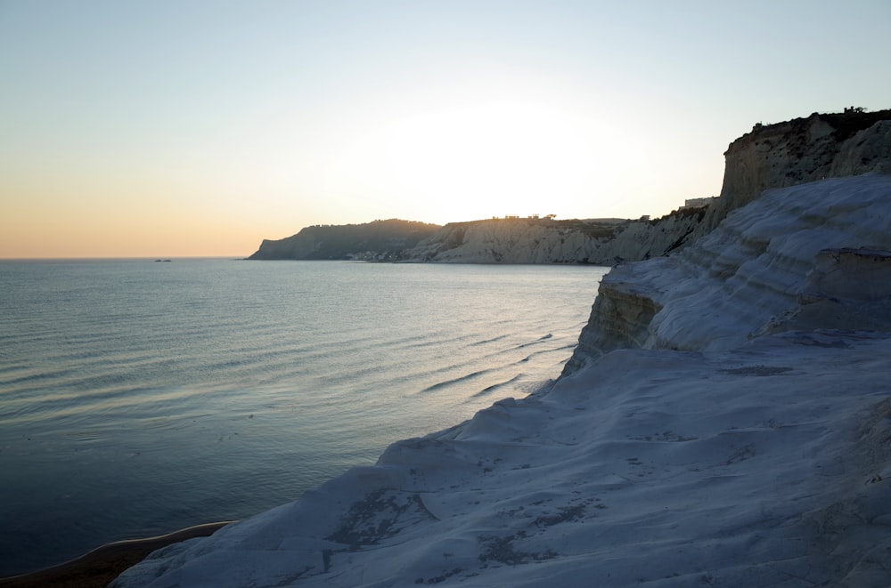 a snowy beach with a body of water and a hill in the background