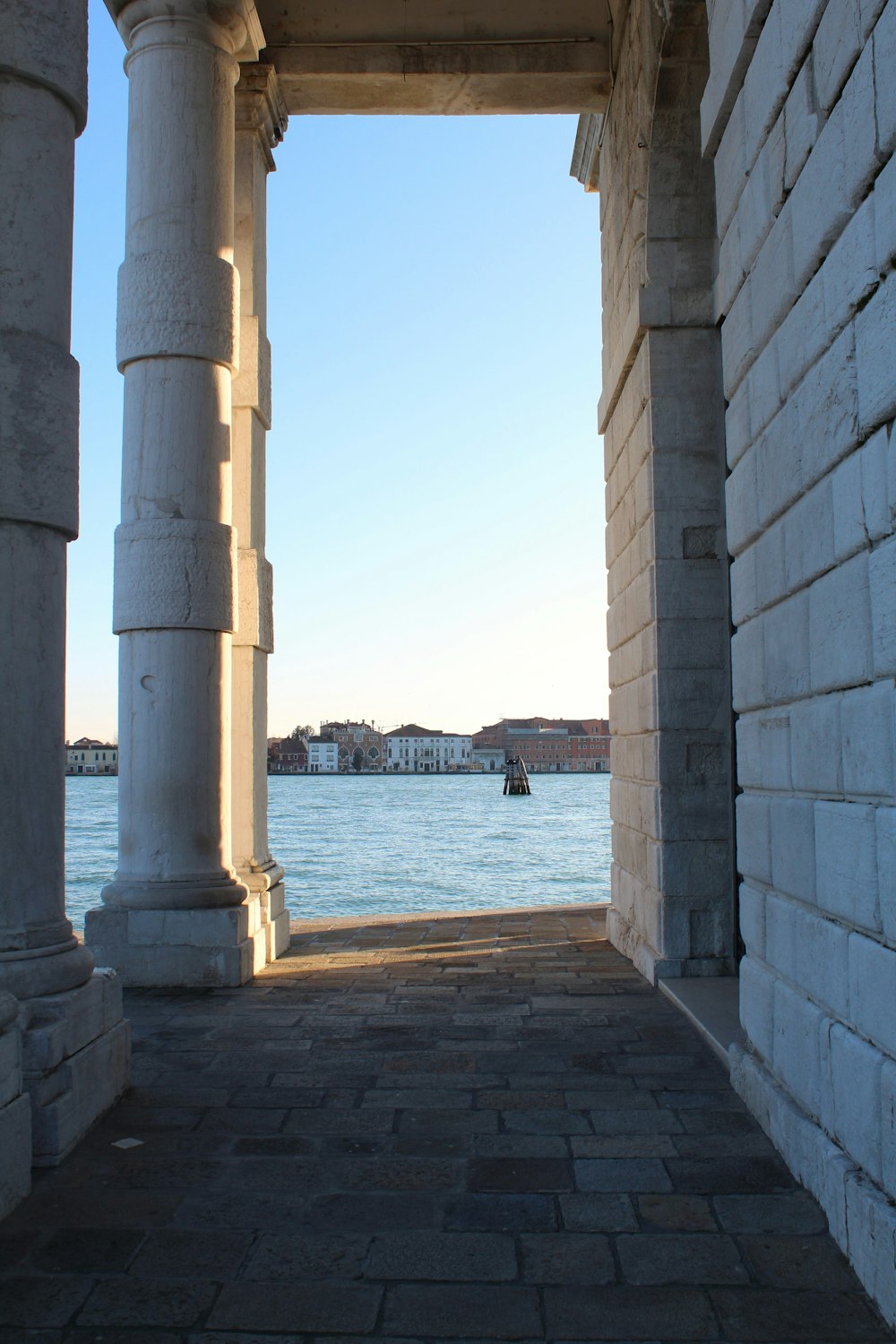 a stone walkway with pillars and a body of water in the background