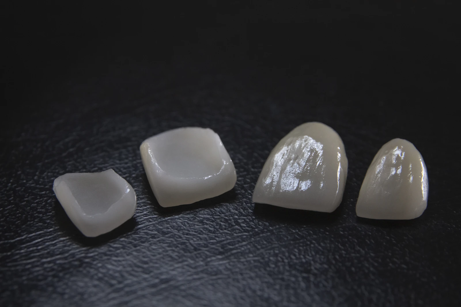 Four ceramic dental crowns on a dark surface
