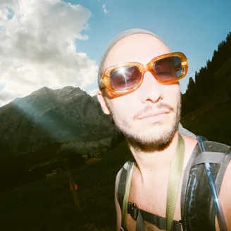 Person hiking wearing durable, scratch-resistant sunglasses with a scenic mountain background.